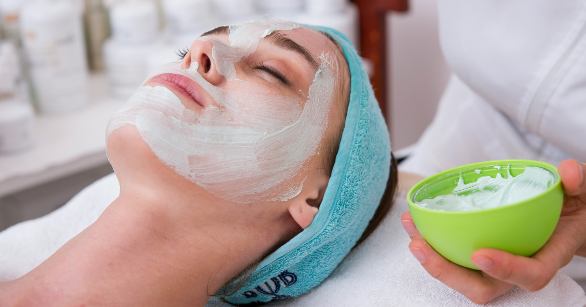 A woman gets a facial using a white paste in a container