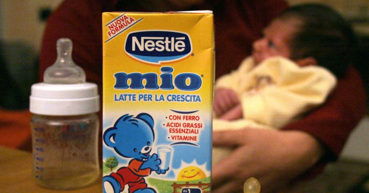 Photo of a bottle and box of Nestlé Mio baby milk in front of a mother holding a baby