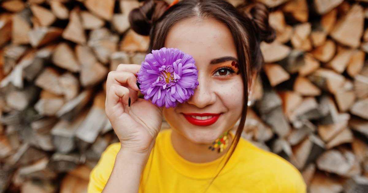 A woman holding an aster flower near her eye. (Representative Cover Image Source: Freepik | AS Photo family)
