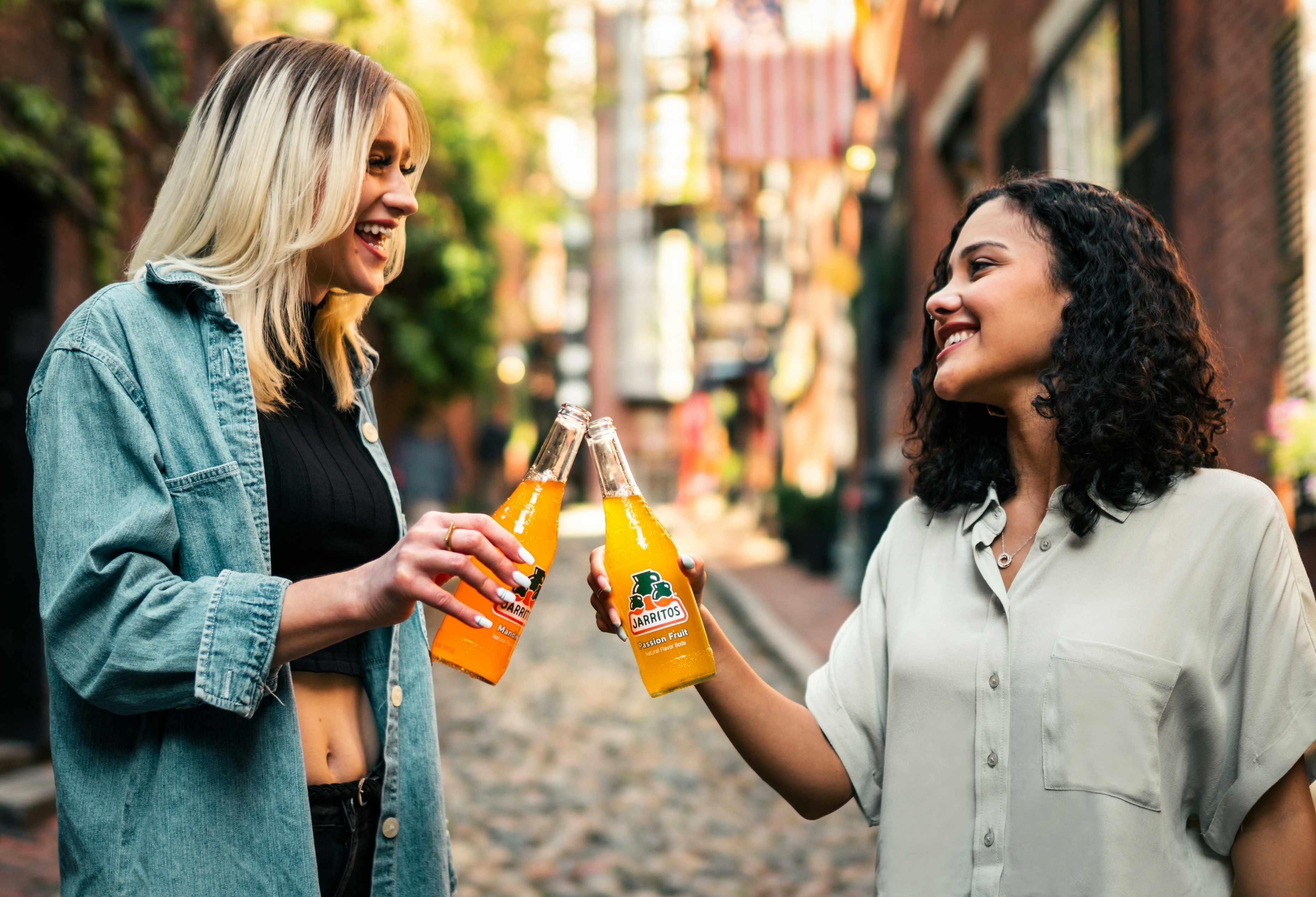 Two smiling women drink Mexican soda together.