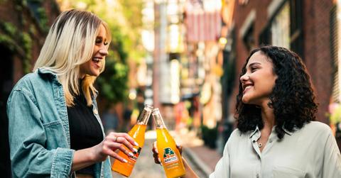 Two smiling women drink Mexican soda together.