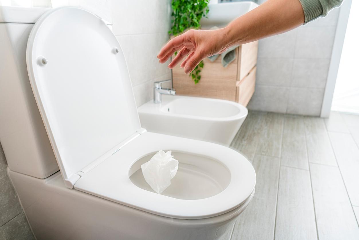 A person throws a balled-up paper towel into a toilet with the lid open.