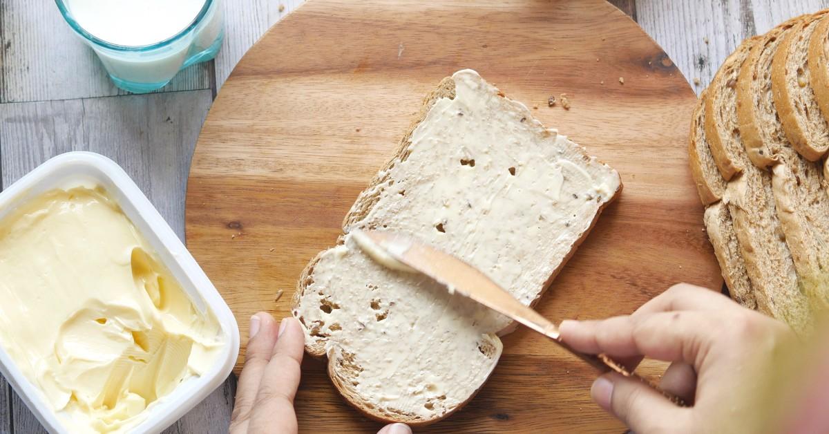 A hand holding a knife spreads a butter like substance on bread