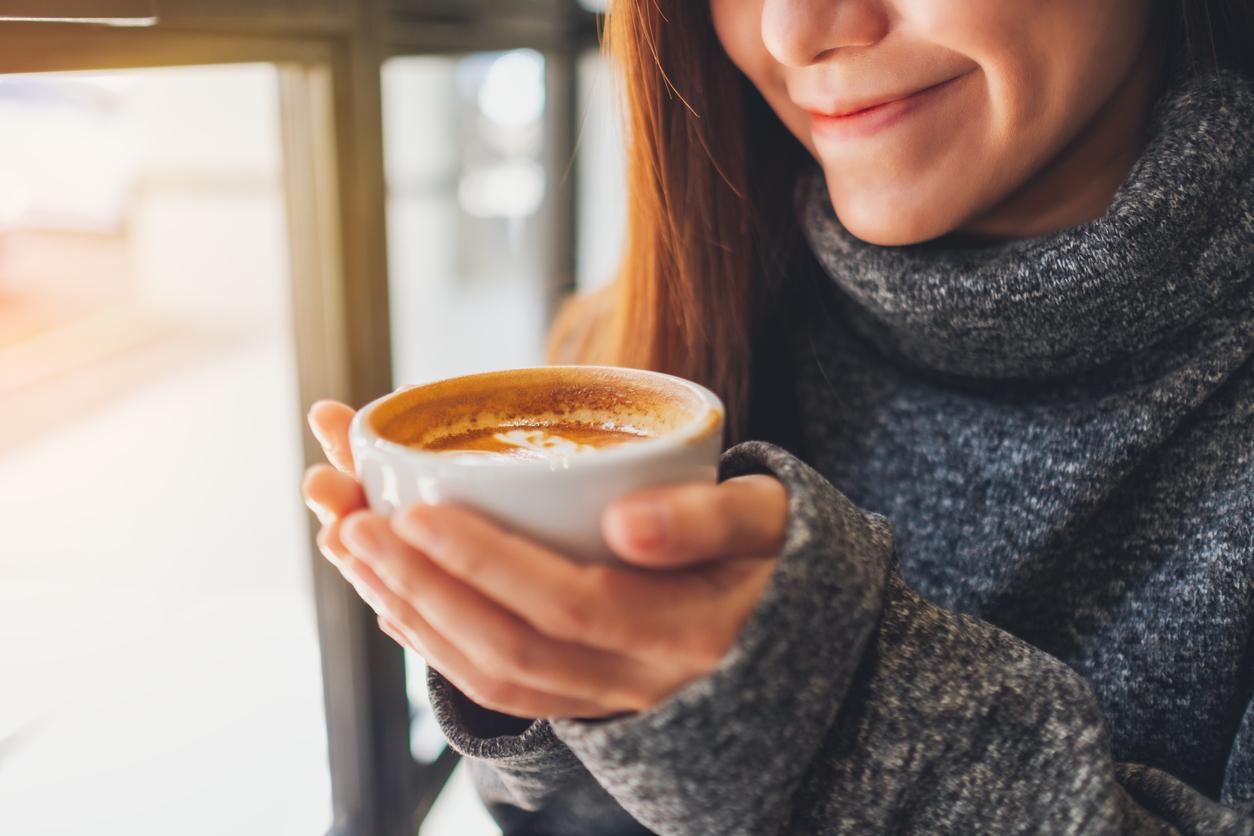 A woman wearing a sweater smiles down at her cup of coffee. 