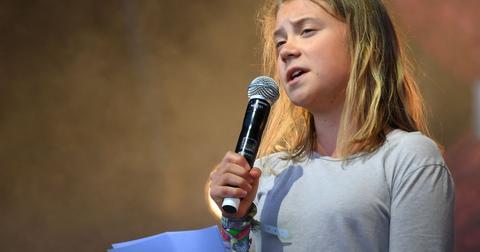 Greta Thunberg holds a microphone to her mouth and a purple piece of paper while giving a speech.