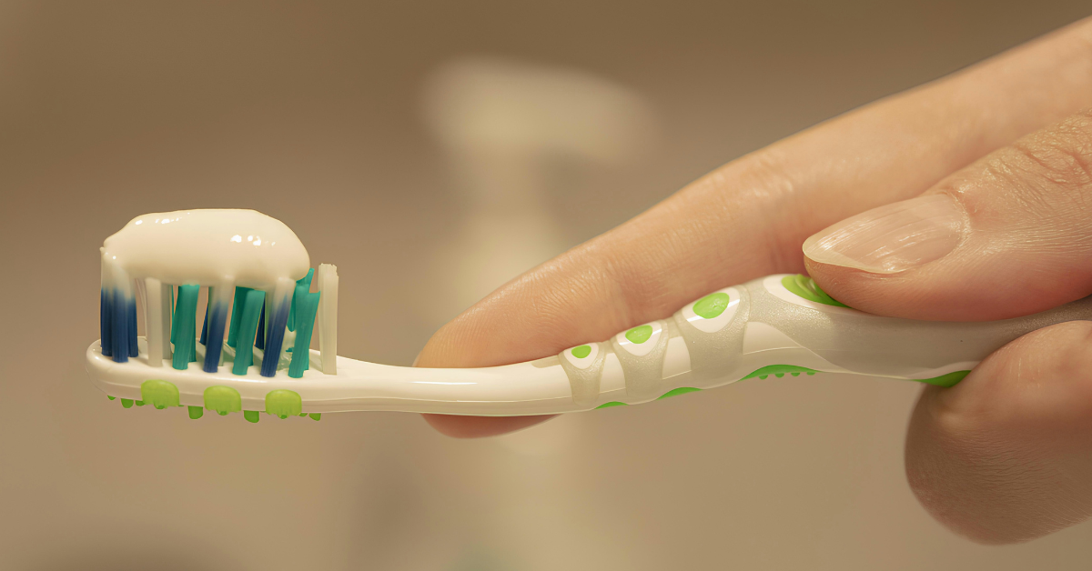 Closeup of white toothpaste on a toothbrush being held by a woman