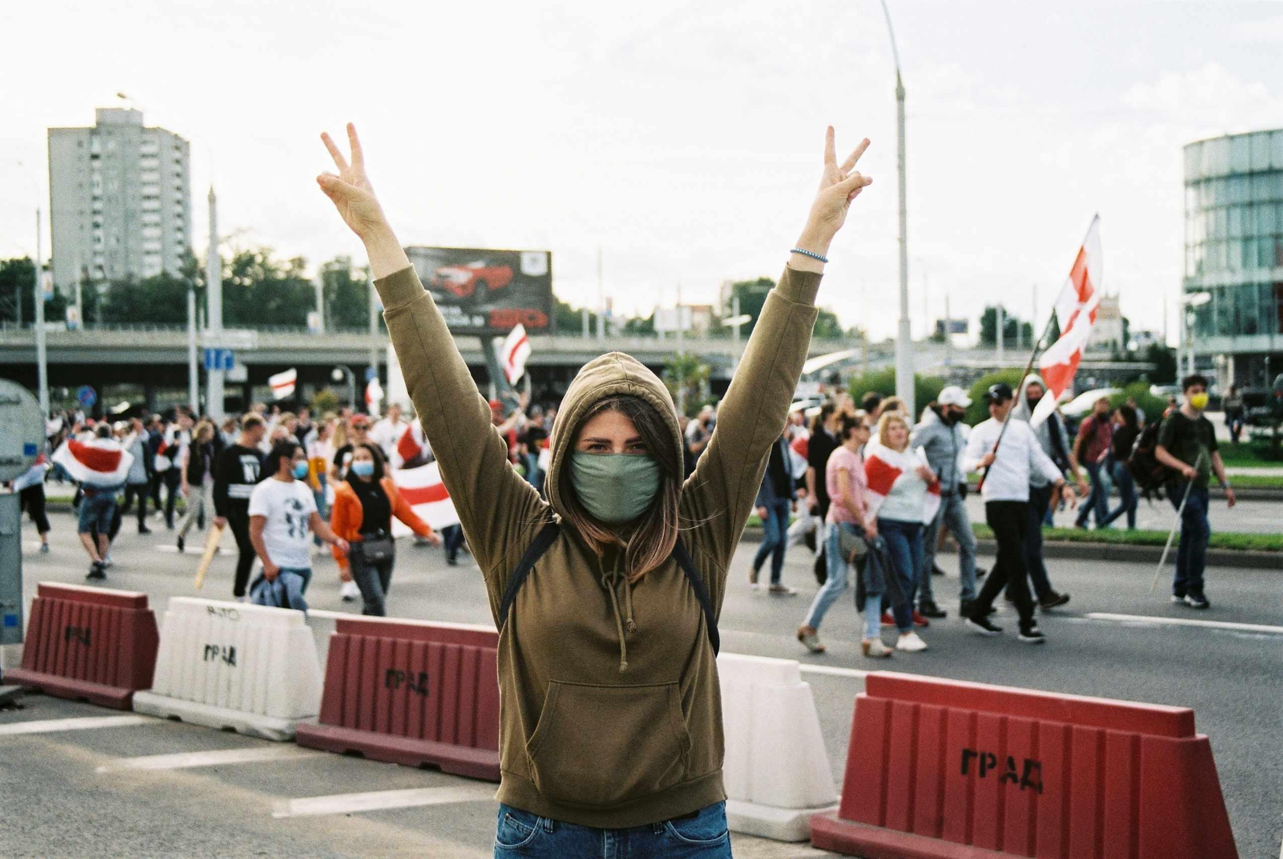 A woman stands with peace signs in front of a protest.