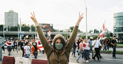 A woman stands with peace signs in front of a protest.