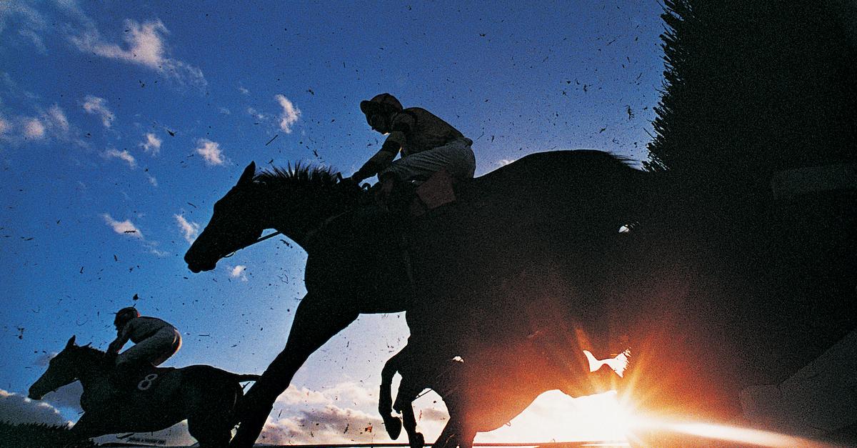 A backlit photo of jockeys riding horses.