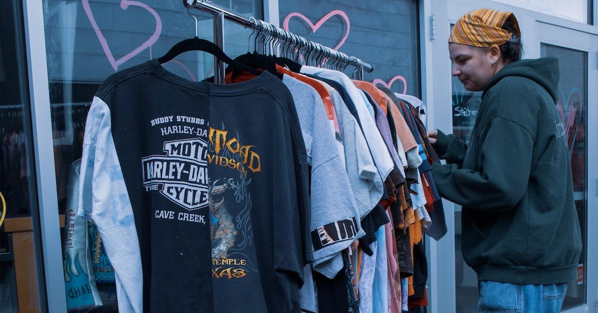 Person browses an outdoor rack of upcycled T-shirts.