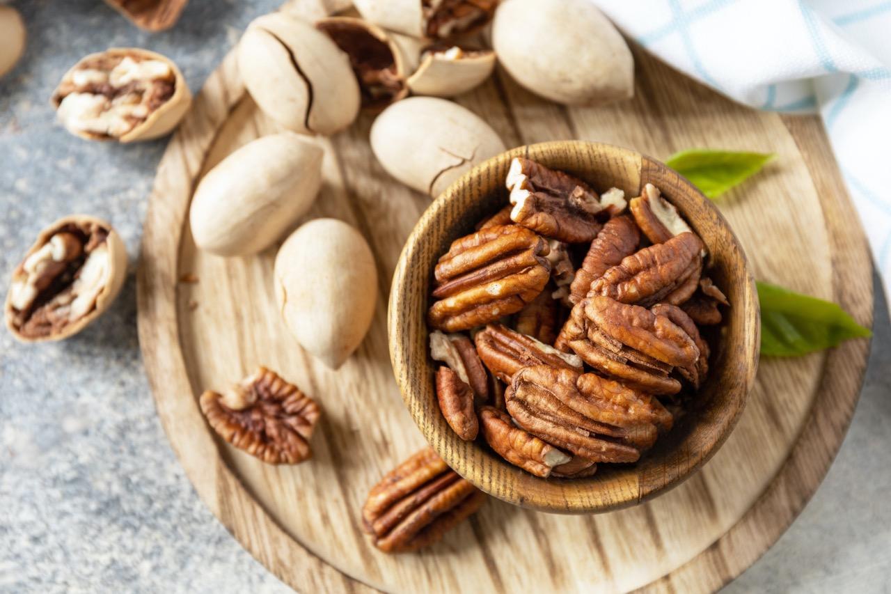 Pecans in a small wood bowl surrounded by pecan shells.