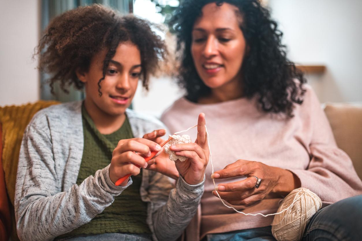 Two people sitting on a couch and working on a crochet project together.