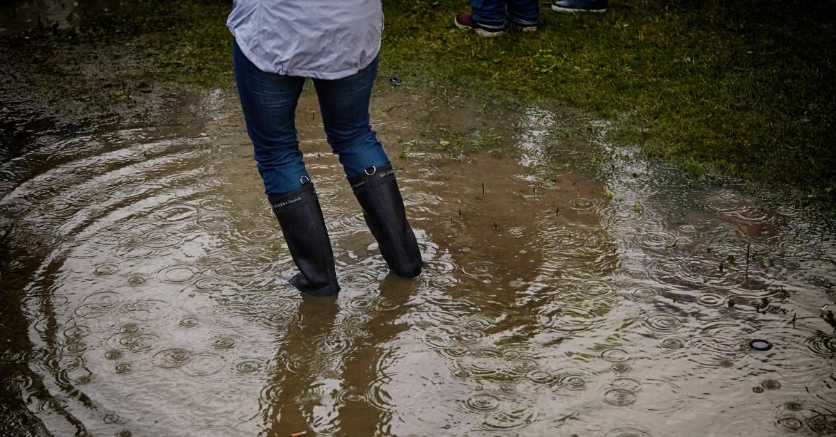 A woman stands in the middle of flood waters while wearing rainboots over her pants