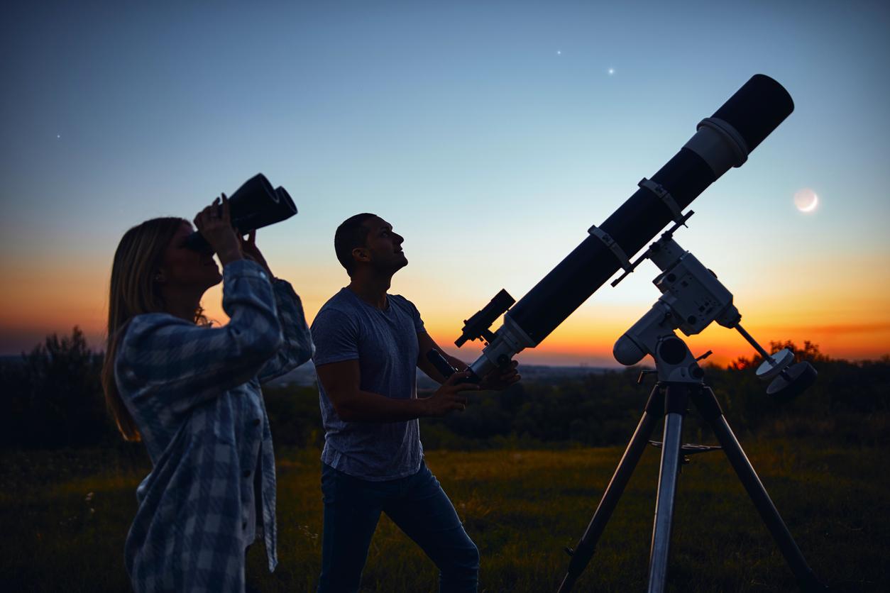 One person is using binoculars to view the night sky and the other is using a telescope.