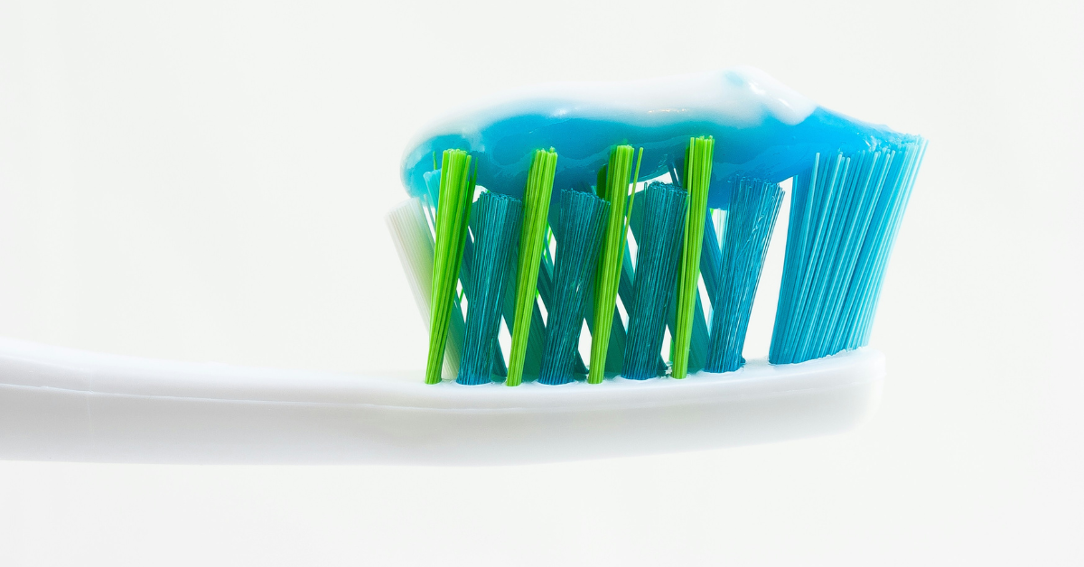 A white toothbrush with blue and green bristles is topped with blue and white toothpaste