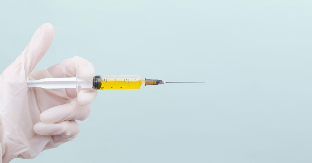 A gloved hand holds a syringe filled with yellow liquid