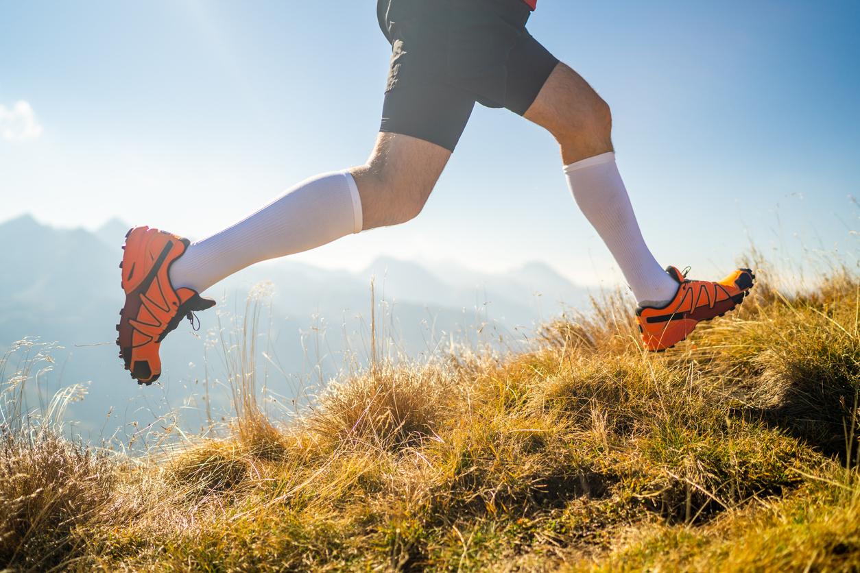 A person appears running on a mountain trail while wearing white compression socks.