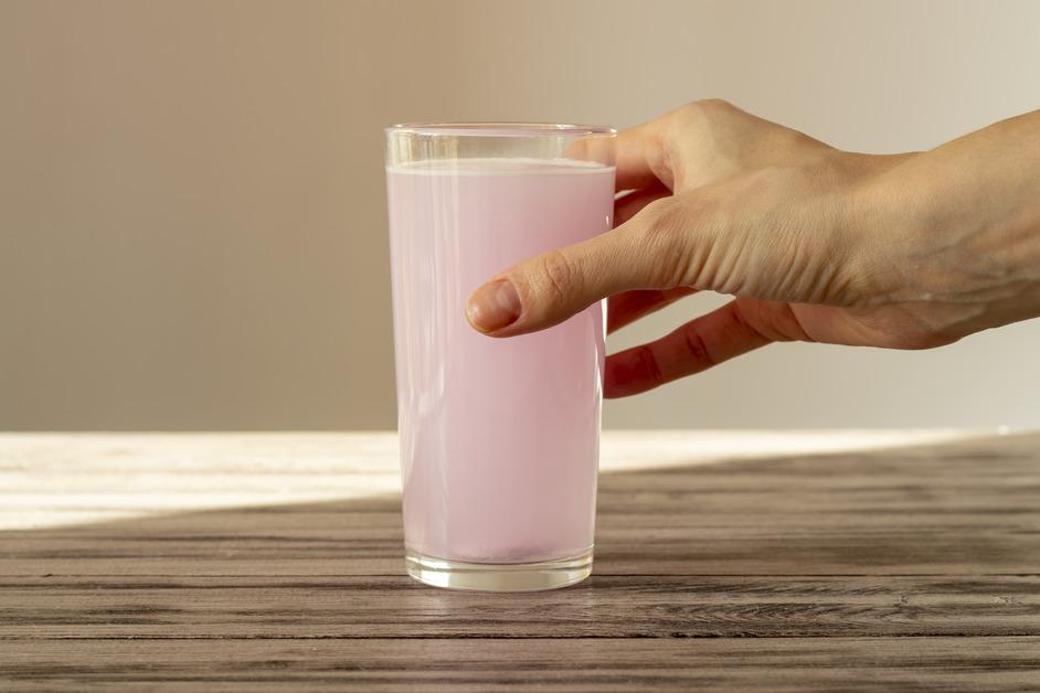 A hand places a glass of pink water on a wooden table.