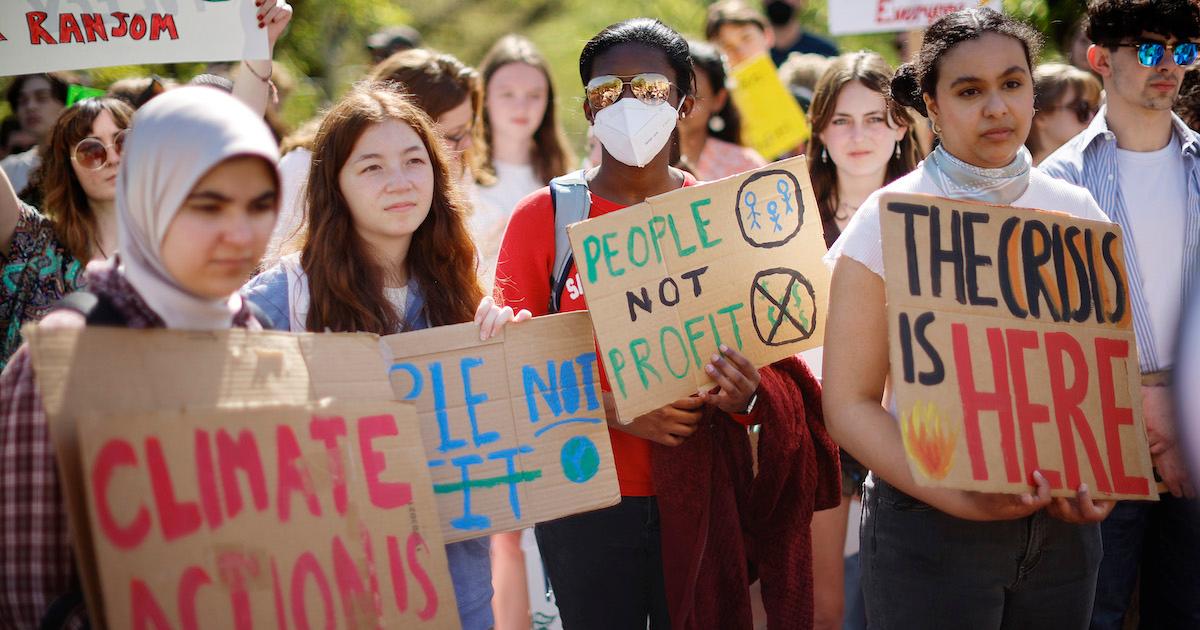 Young climate activists hold posters reading “climate action,” “people not profit,” and “the crisis is here.”
