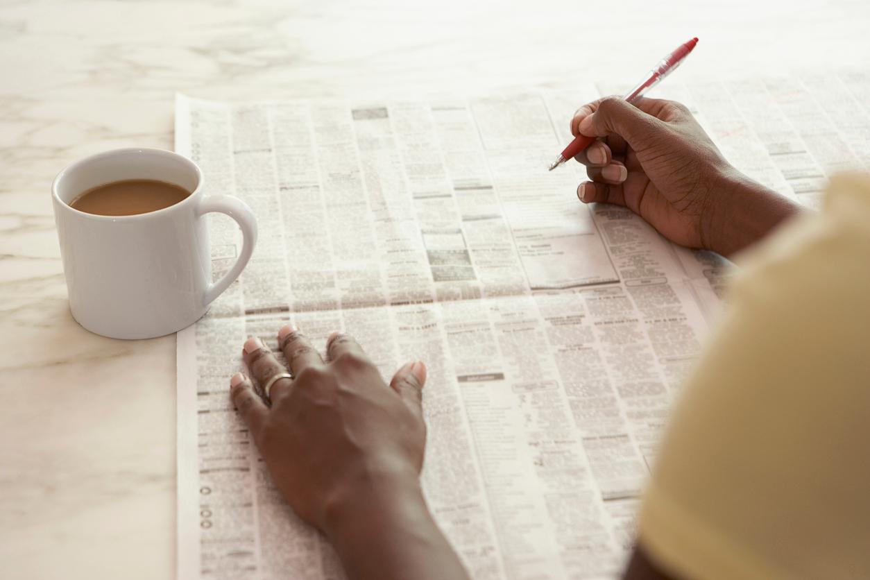 Person reading the newspaper and marking ads while they drink coffee.