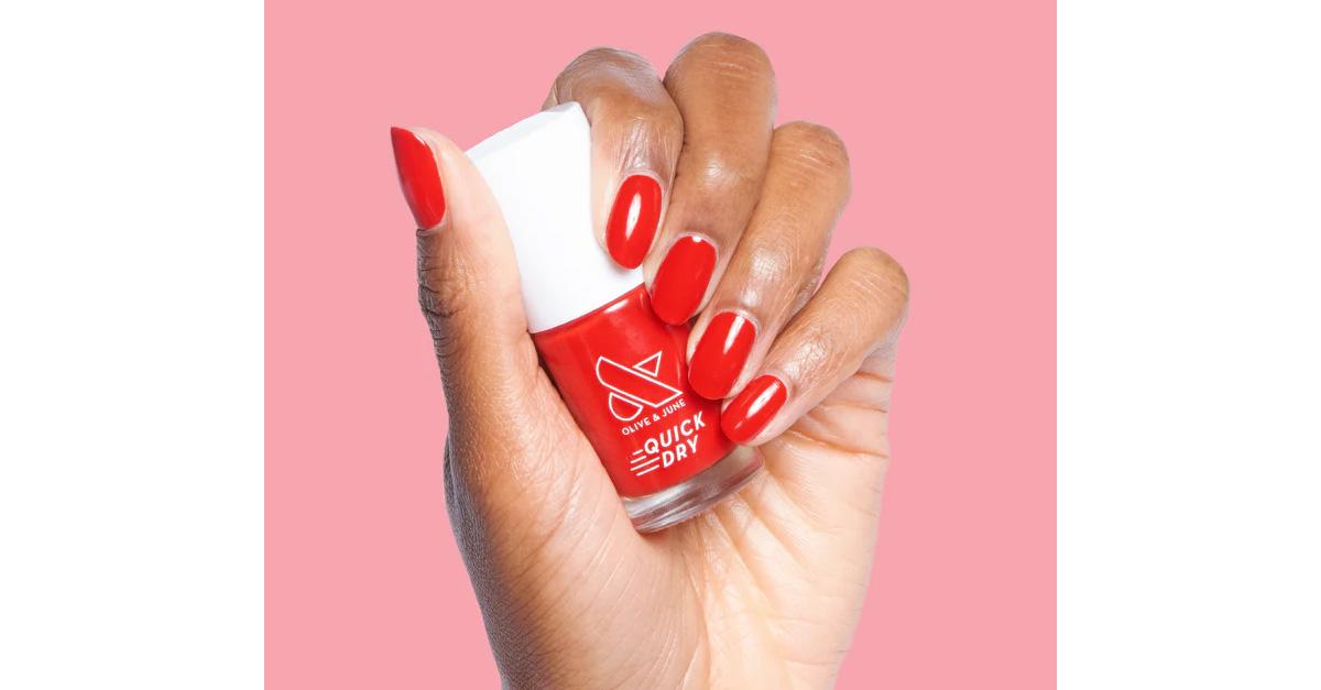 a hand holding a bottle of red nail polish on a pink background