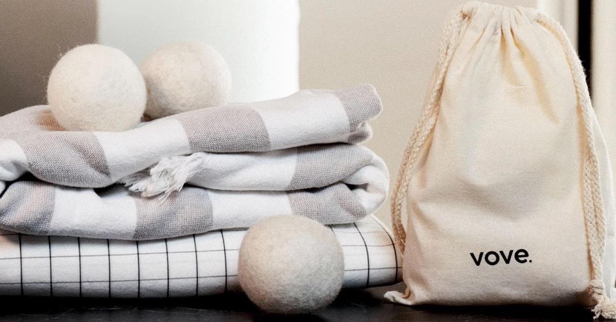 Three dryer balls sit near a pile of towels, along with a beige storage bag that says vove.