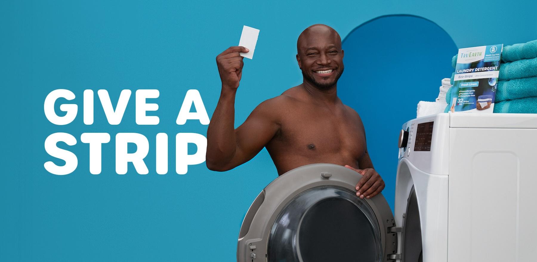 Taye Diggs is topless and smiles, while standing nude with a washing machine blocking his body, and holds up Tru Earth's laundry eco-strip