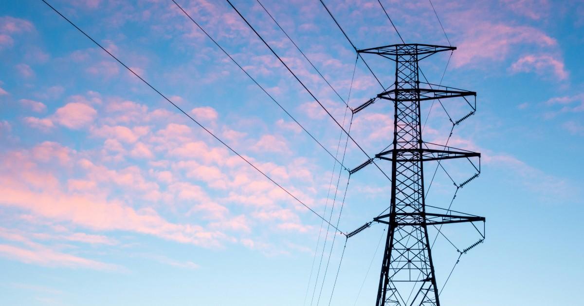 A high tension powerline appears black against a pink and blue sky