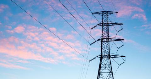 A high tension powerline appears black against a pink and blue sky