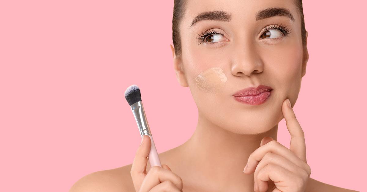 woman applying foundation with a brush on a pink background