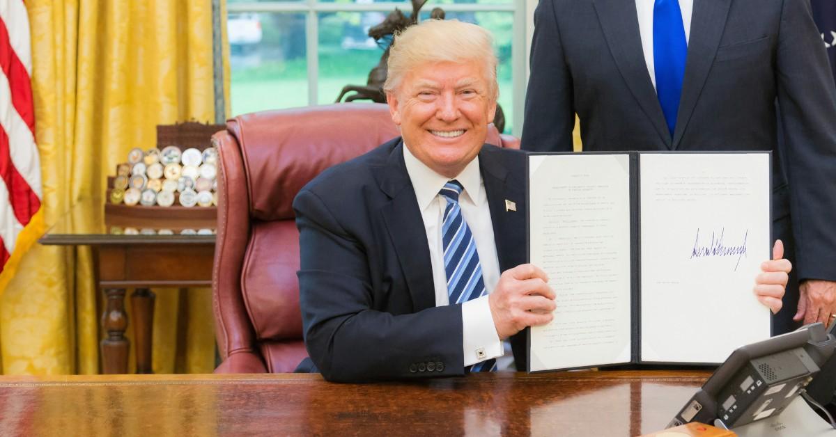 Donald Trump smiles while holding up a paper with his signature on it
