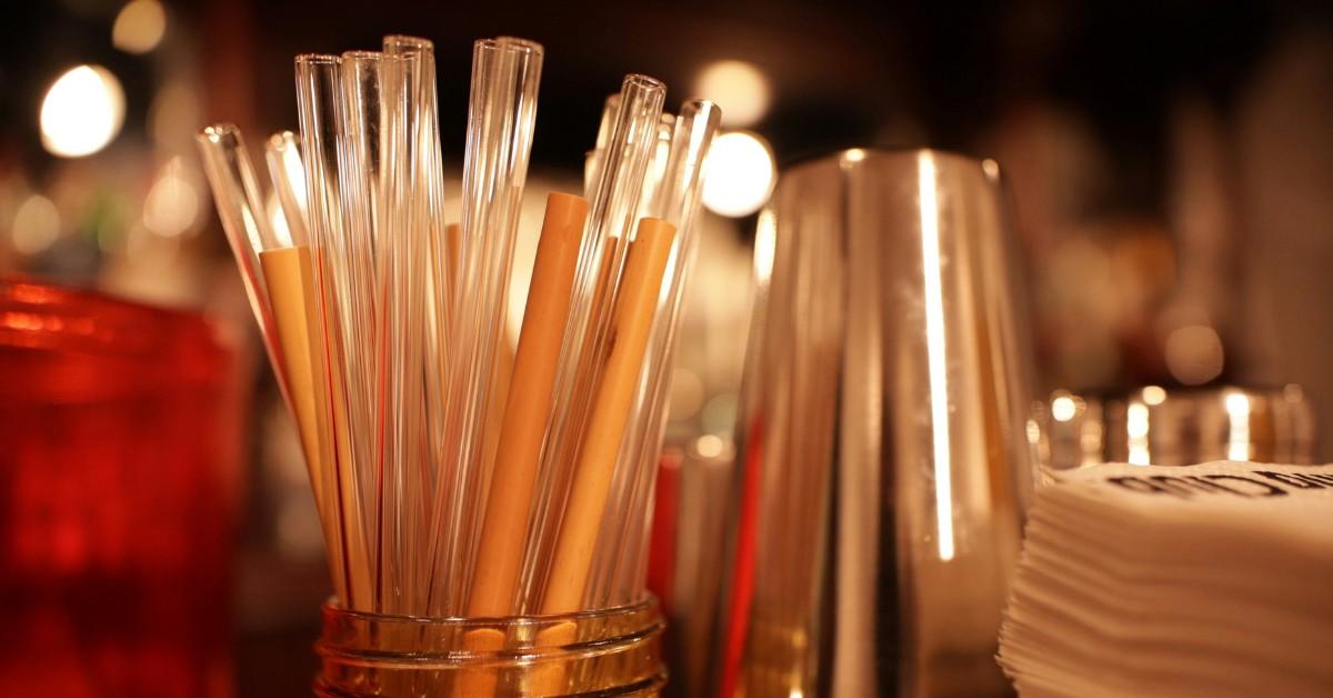 A glass jar holds a collection of straws that include some glass ones and some cardboard ones