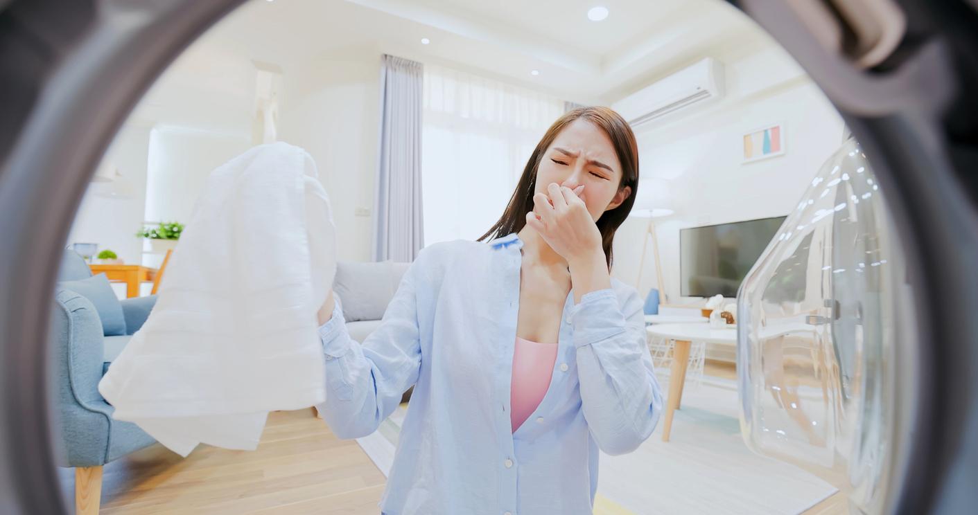 A woman plugs her nose due to the offensive odor of a sheet she removes from the dryer.