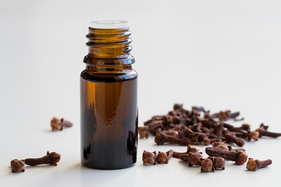 An open container or clove oil with cloves on the side. 