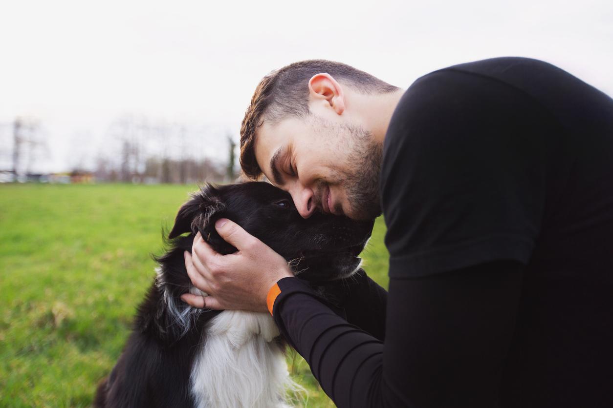 A man in a black shirt hugs his black dog and presses his head against the dog's forehead.