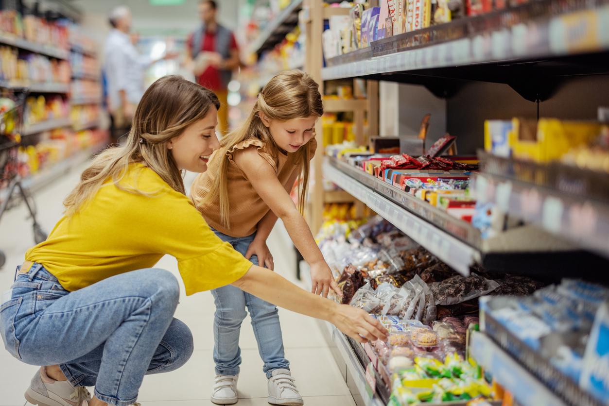 A mother and daughter pick out sweets from a grocery store candy aisle.