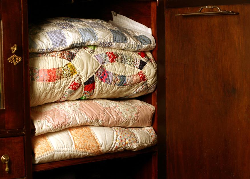 Four quilts sit stacked in a wooden closet.