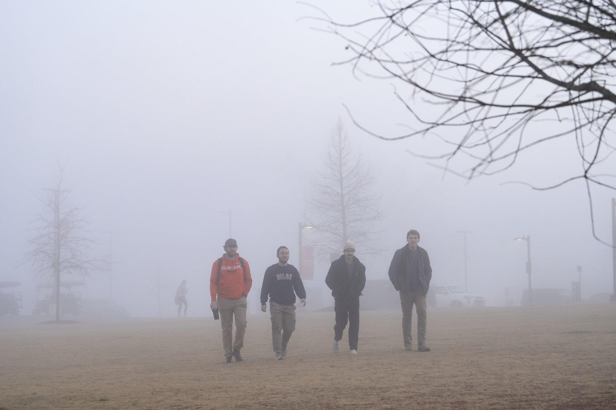 Four Clemson University students walk together in an open field on the Clemson campus.