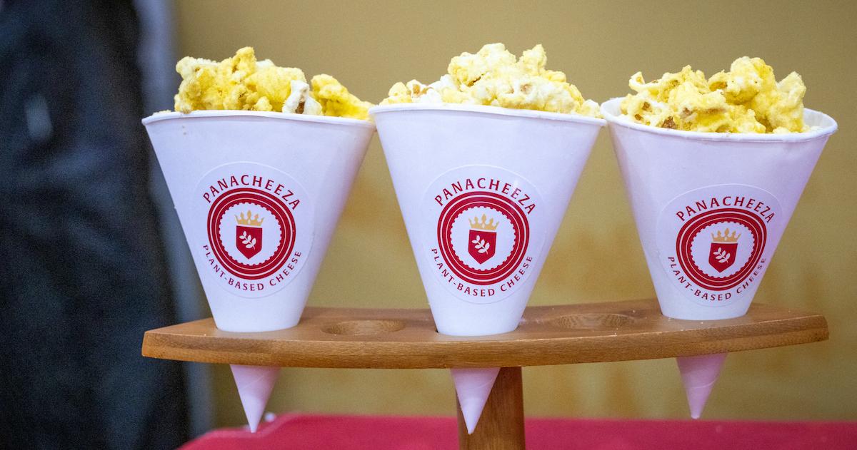 Three cups of popcorn topped with vegan Parm, in cups with Panacheeza's logo