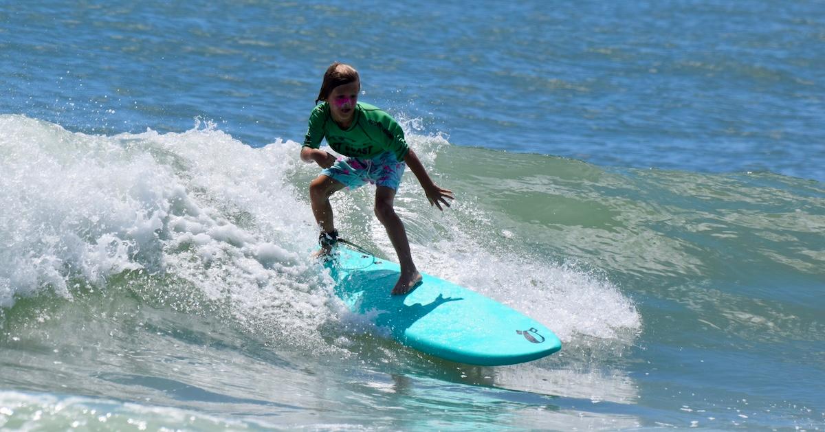 Child rides a wave on a turquoise Rock-It Surf surfboard