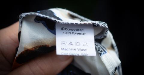 Close-up photo of a hand holding 100% polyester fabric in front of a black background