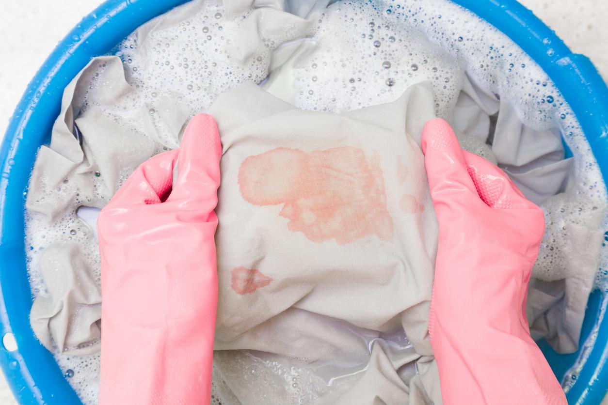 Close up view of a pair of pink-gloved hands stretching out a stained piece of fabric in a blue bucket of soapy water.