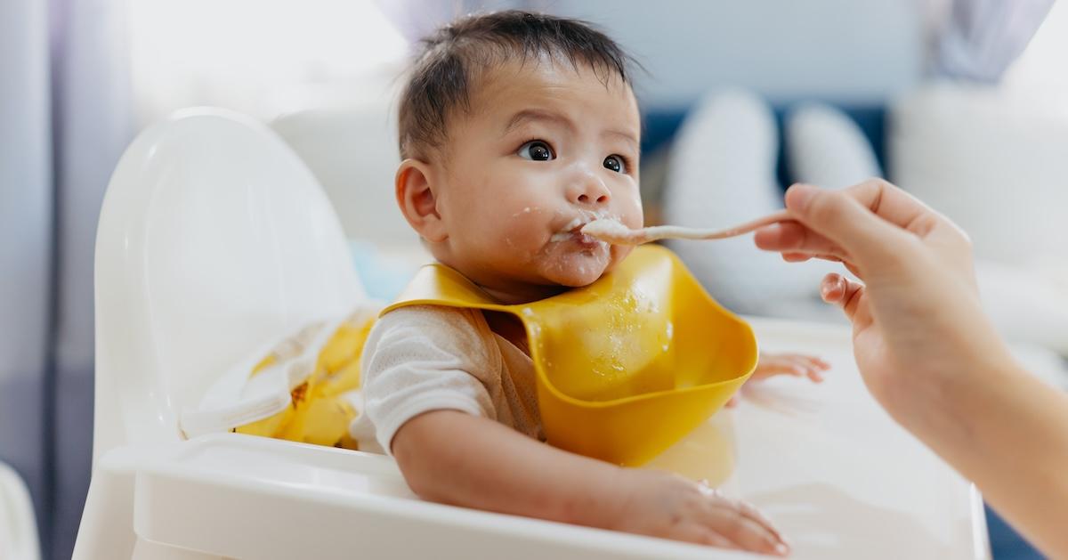 Mother is out of frame and feeds her baby boy using a spoon 