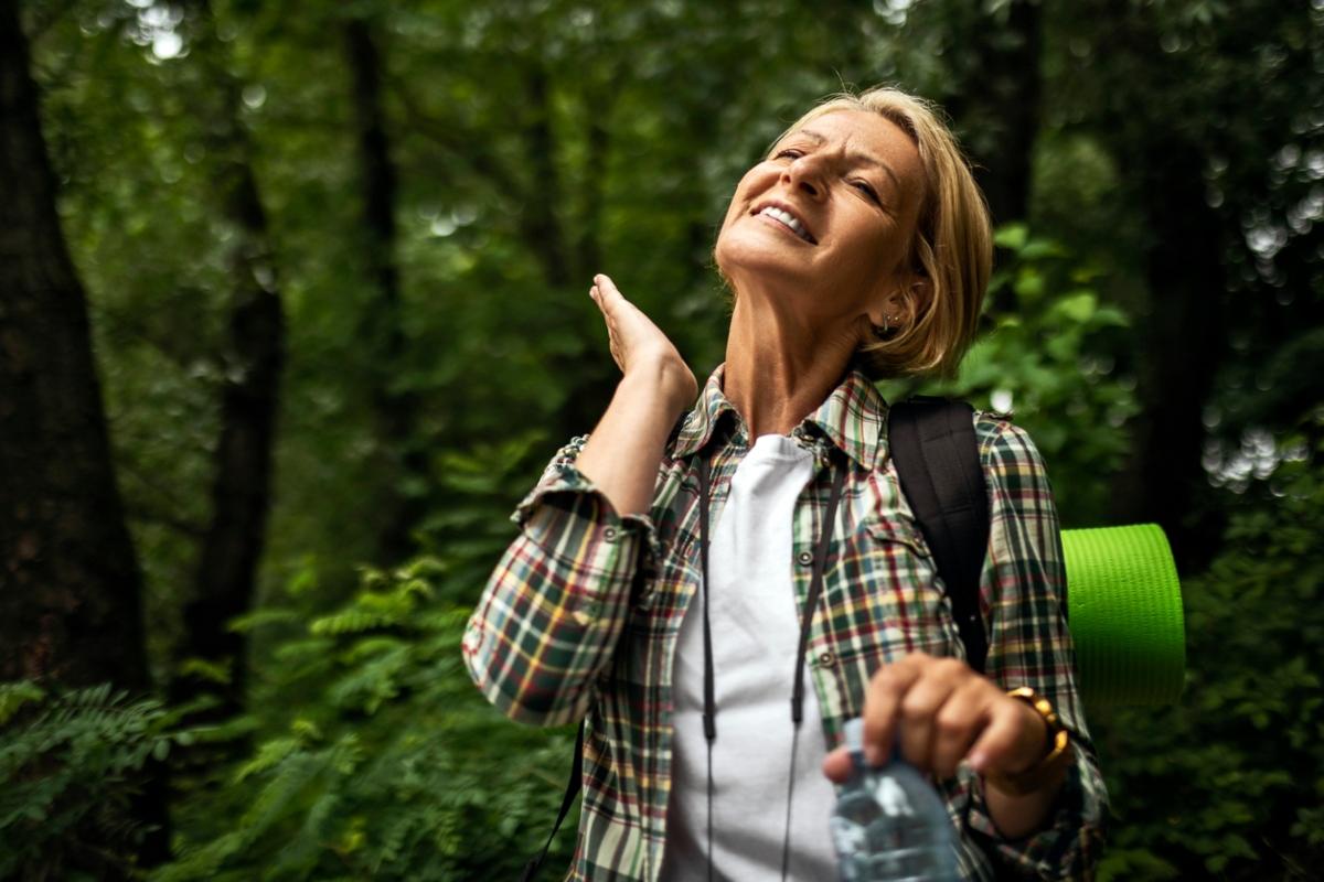 Woman in plaid shirt in the woods about to slap a mosquito.