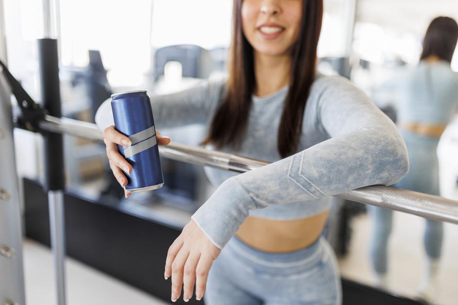 A woman leans on a bar while wearing a blue workout set and holding an energy drink.