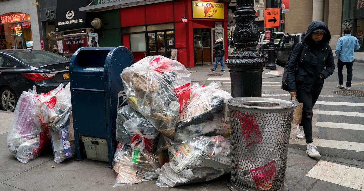 Pedestrians walk past bags of trash on a sidewalk in Lower Manhattan