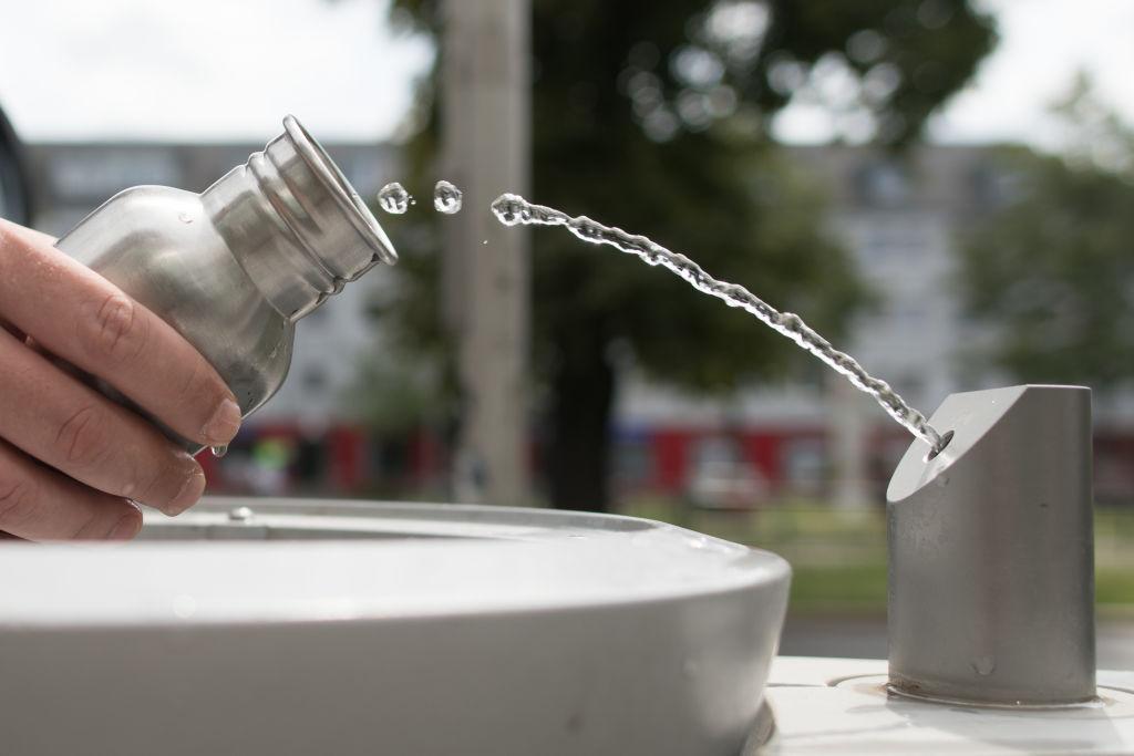 A park-goer fills his reusable metal drinking bottle with water at a stainless steel refill station water fountain in Germany.