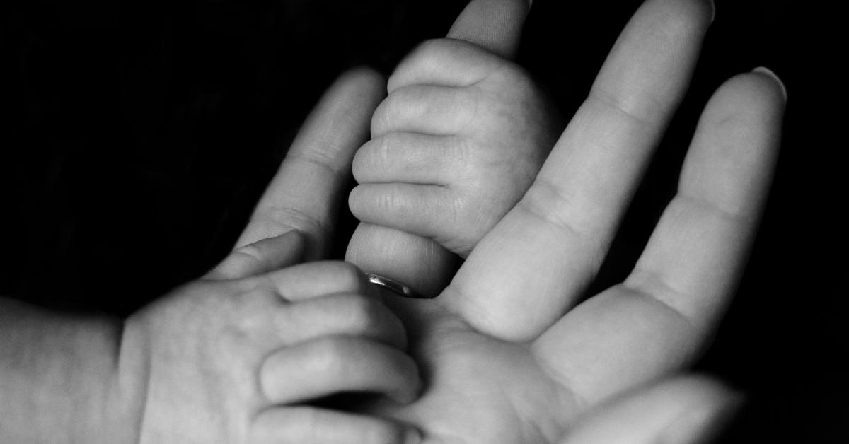 Parent holding the hand of their small child in black and white. 