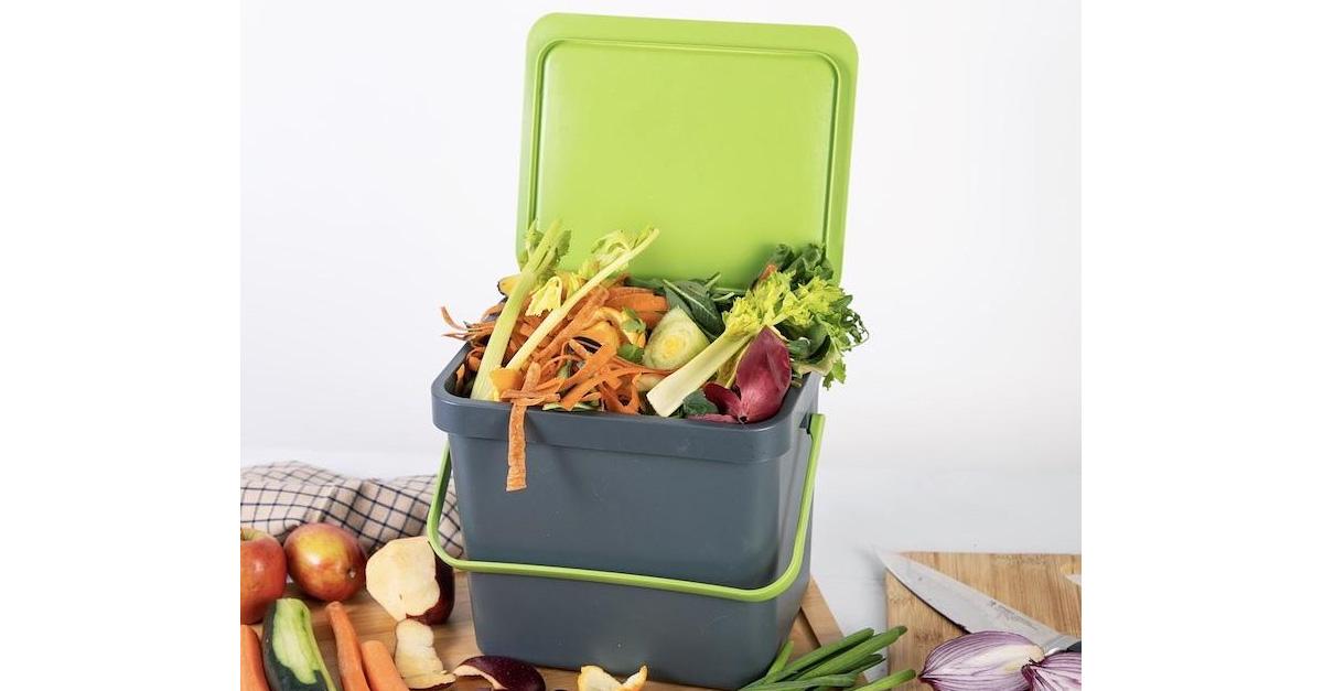 Green and gray compost bin with handle and food scraps inside and around it.