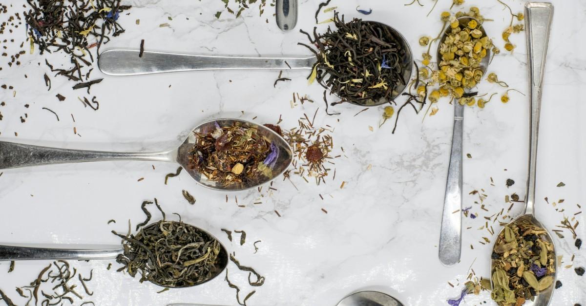 Spoons holding a variety of loose tea leaves lay on a table